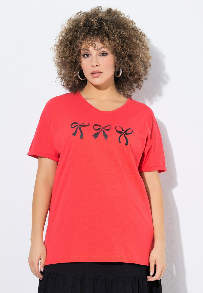 T-shirt en coton rouge avec un col en V et des manches courtes, présentant trois motifs de nœuds noirs sur le devant. Texture douce, coupe décontractée.