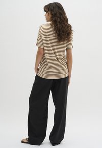 Chemise à manches courtes rayée en beige et marron, coupe décontractée, associée à un pantalon noir ample, mettant en avant un design simple et décontracté.