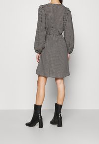 Svartvit houndstooth-mönstrad klänning med långa puffärmar, åtdragen i midjan och utsvängd nederdel; kombinerad med svarta klackstövlar.