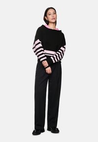 Black hoodie with pink striped sleeves, featuring a pink hood. Paired with high-waisted black trousers and chunky black shoes.