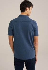 Camisa polo de manga corta para hombre en azul oscuro, fabricada con un tejido texturizado. Cuenta con un cuello, un detalle sutil en la costura trasera y aperturas laterales en el dobladillo.