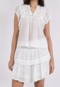 Donna che indossa un abito bianco senza maniche con volant e dettagli in pizzo, caratterizzato da un scollo a V e una gonna a strati.