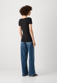Svart t-shirt med kort ärm och fyrkantig utskärning, i kombination med löst sittande blå denimjeans. Slät textur och avslappnad design.