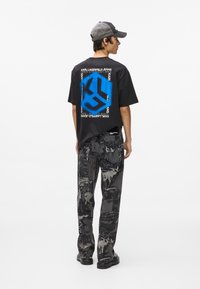 Μαύρο βαμβακερό t-shirt με γαλάζιο σχέδιο και εκτύπωση λογότυπου στο πίσω μέρος. Γκρι τζιν παντελόνι με σχέδιο ολοκληρώνει την εμφάνιση, συνδυασμένο με μαύρη υπόδηση.