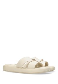 Ljust beige slide-sandaler har en formad design med korsade remmar, en slät yta och en platt sula för komfort. Gyllene detaljer synliga.