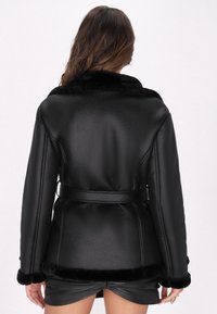 Giacca di pelle nera con colletto e polsini in pelliccia, vita aderente e finitura textured. Presenta una vestibilità su misura e una silhouette fluida.