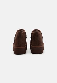 Stivaletti alla caviglia in suede marrone con superficie texture, colli imbottiti e suola piatta in gomma. Chiusura con lacci e design minimal.