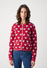 Punainen neulecardigan, jossa on vaaleanpunainen sydänkuvio, pyöreä pääntie, napitus ja kaksi etutaskua.