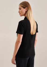 Czarna koszulka polo z krótkimi rękawami, z klasycznym kołnierzykiem i miękką fakturą. Prezentowana z tyłu, w połączeniu z prostymi spodniami.