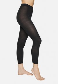 Schwarze Leggings aus dehnbarem Material, mit einer glatten Textur, hohem Bund und einer engen Passform, die sich an den Knöcheln verjüngt.