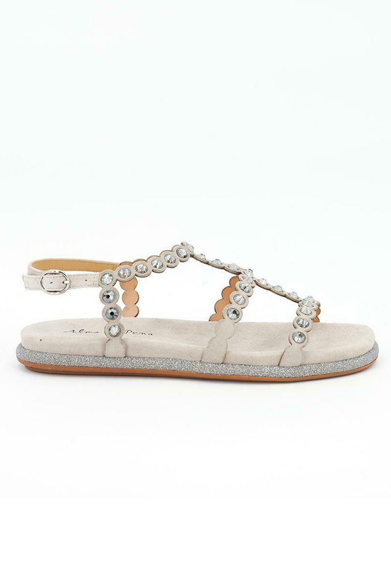 Sandalia plana beige con tira en el tobillo, decorada con strass transparentes redondos y acentos de purpurina plateada en el borde de la suela.