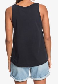 Zwart tanktop met een klassieke ronde hals en mouwloze uitvoering, gecombineerd met lichte denim shorts met opgerolde pijpen.