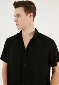 Fekete, rövid ujjas póló, texturált anyagból, gombos nyitással és klasszikus gallérral. Egyszerű és minimalista dizájn.