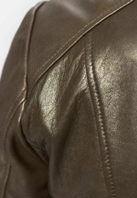 Bruine leren jas met schouderdetail en een glanzende afwerking. Kenmerkt zichtbare stiksels en een soepele textuur. Naad en ontwerplijnen zijn prominent aanwezig.