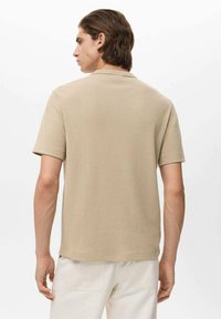 Tricou scurt, bej, cu mânecă scurtă, cu un finisaj texturat, de tip crew neckline și cu tiv drept. Țesătura pare moale și ușoară.