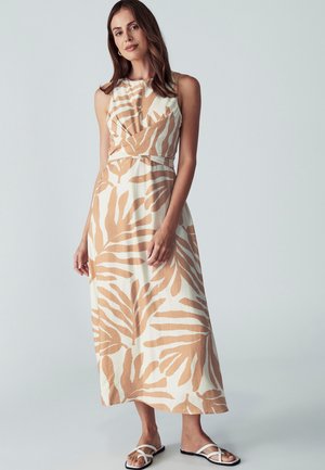 Maxi sukienka w kolorze kremowym z jasnobrązowymi wzorami liści. Posiada dopasowaną górę, bez rękawów oraz wcięcie w talii. Noszona z płaskimi sandałami.