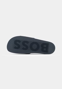 Fekete gumitalp vízszintes barázdákkal és domború "BOSS" felirattal. Simább textúra, enyhén ívelt forma. Minimalista dizájn.