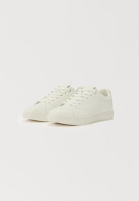 Balta pora žemų lygiais batų su raišteliais ir tekstūruotais guminiais padais ant balto fono.