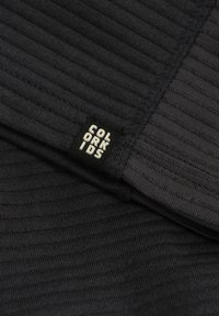 Svart ribbat tyg med en strukturerad yta, med en sydd etikett märkt "COLOR KIDS." Övergripande slät yta med subtil mönstring.