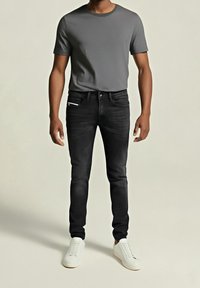 Svarta slim fit jeans med en klassisk fem-fickorsdesign, kombinerat med en grå t-shirt med kort ärm och vita sneakers. Slät textur.