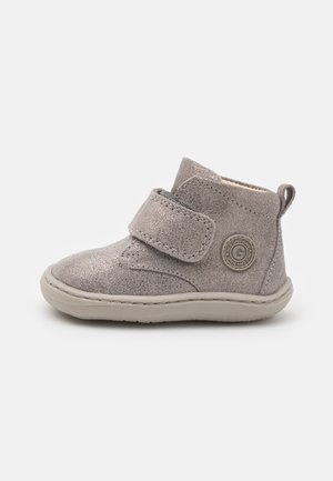 Stivaletto alla caviglia in tessuto grigio con una striscia in velcro, punta arrotondata e suola in gomma leggera. Presenta un dettaglio a logo circolare sul lato.
