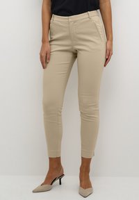 Pantaloni beige su misura con una vestibilità slim, dotati di tasche laterali, una vita senza cuciture e una finitura in tessuto elasticizzato e liscio.