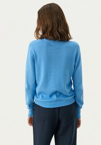 Zils adīts džemperis ar apaļu kakla izgriezumu, ribotām piedurknēm un apakšmalu. Aizmugurē ir gluda tekstūra un pieguļošs dizains. Saskaņots ar tumšiem biksēm.