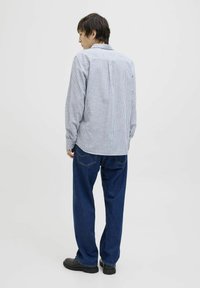 Camisa de botones de rayas en azul y blanco, con un yugo en la parte trasera y mangas largas, combinada con unos vaqueros oscuros de corte holgado y zapatos negros.