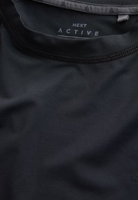 T-shirt de sport noir avec un gros plan sur l'encolure et le col cousu, montrant l'étiquette de marque imprimée "NEXT ACTIVE" à l'intérieur du col.