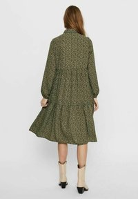 Abito lungo a maniche lunghe, a strati, di colore verde scuro con un delicato motivo floreale. Realizzato in tessuto leggero, presenta un colletto e arriva a metà polpaccio.