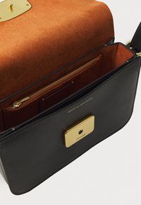 Schwarze Lederhandtasche mit einem goldfarbenen Verschluss. Das Innere ist mit einem braunen Suede-Futter ausgestattet, verfügt über eine Reißverschlusstasche und Kartenfächer zur besseren Organisation.
