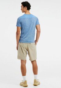 Modrá ľahká športová tričko s krátkymi rukávmi, skombinovaná s béžovými šortkami. Model má na sebe béžové tenisky a biele ponožky.