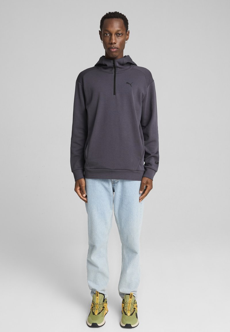 Sudadera de felpa gris oscuro para hombre con media cremallera, logotipo negro, combinada con jeans rectos de color azul claro y zapatillas con detalles amarillos.