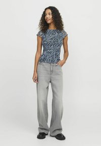 Top a maniche corte blu e nera a righe zebra, jeans grigi a gamba larga e scarpe platform nere. Vestibilità ampia con un motivo testurizzato.