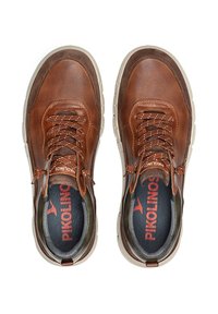 Zapatillas de cuero marrón con paneles de malla, cordones redondos, cuello acolchado y suelas de goma. En el interior destacan los detalles de la marca 'Pikolinos' en rojo.