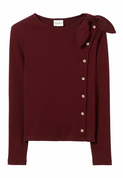 Top lungo bordeaux a maniche lunghe realizzato in tessuto a coste, con un fiocco sulla spalla e bottoni dorati lungo il lato. Tessuto morbido.