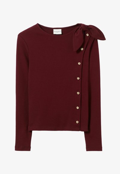 Top lungo bordeaux a maniche lunghe realizzato in tessuto a coste, con un fiocco sulla spalla e bottoni dorati lungo il lato. Tessuto morbido.