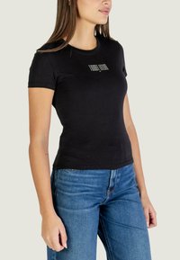 T-shirt nera a maniche corte in cotone, con grafica del logo bianca sul petto. Abbinata a jeans di denim blu.