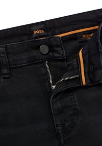Jeans neri con zip argento parzialmente aperta, bottone nero con incisione "BOSS" e etichette arancioni del marchio all'interno della vita.