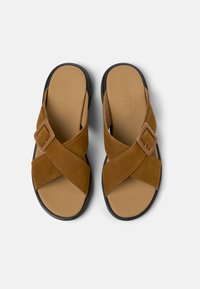 Sandali in suede marrone con fasce incrociate, dotati di dettaglio con fibbia, una soletta imbottita beige e una suola in gomma nera.