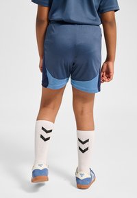 Marina sportshorts med ljusblå sidopaneler, kombinerat med knähöga vita strumpor med svarta chevronmönster och blå skor.