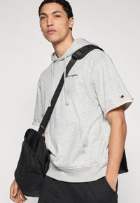 Γκρι φούτερ με κουκούλα, εμπρόσθια τσέπη, κορδόνια ρύθμισης και μανσέτες στα μανίκια. Μαύρη τσάντα ώμου με λεπτομέρεια από δίχτυ. Απλός, καθημερινός σχεδιασμός.