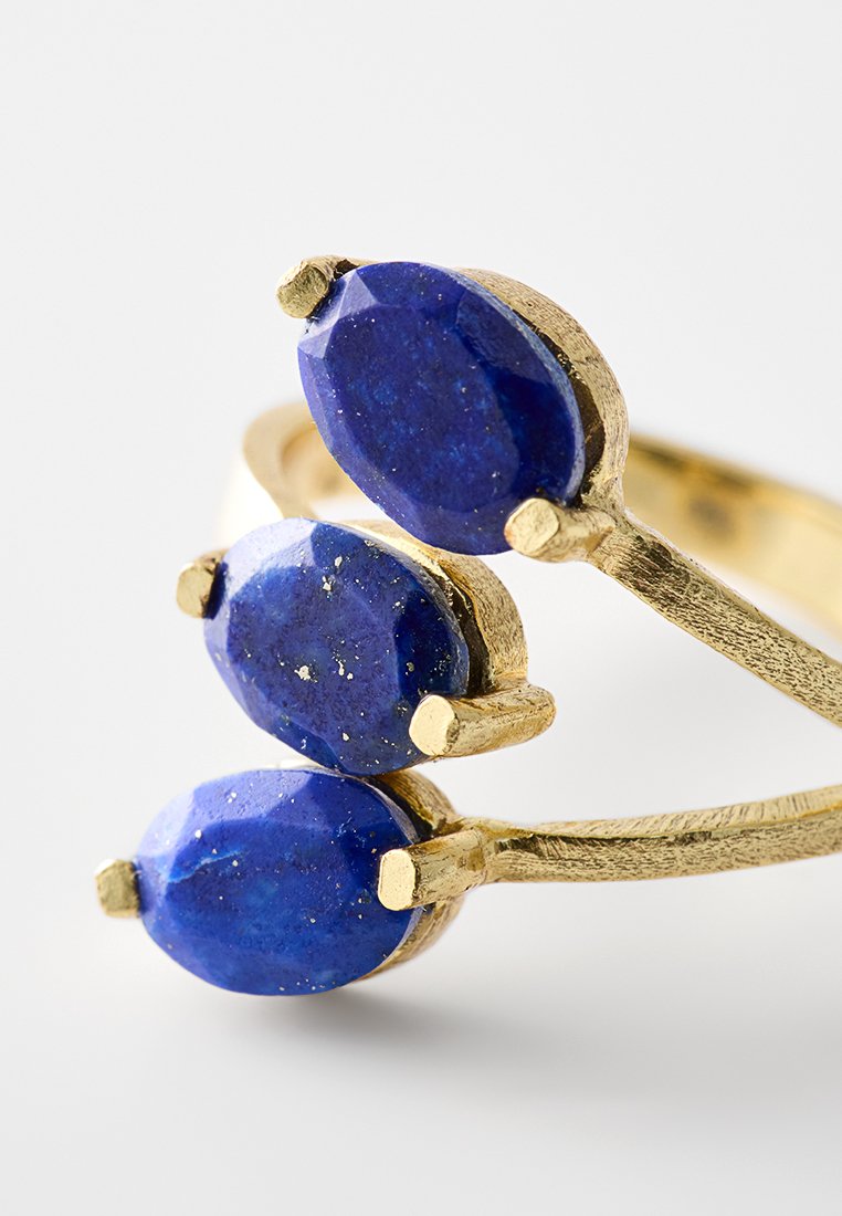 Goldring mit drei ovalen, facettierten, tiefblauen Edelsteinen, die in einer Reihe angeordnet sind, in Krappenfassungen auf einem schlichten Hintergrund.