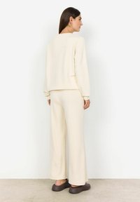 Crèmekleurige, zachte loungewear set met een langemouwen top en wijde broekspijpen, gecombineerd met bruine instappers.