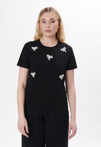 Schwarzes T-Shirt mit sechs kleinen, strukturierten, silbernen Bandapplikationen auf der Vorderseite. Rundhalsausschnitt, kurze Ärmel und eine taillierte Silhouette.