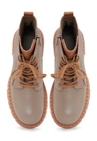 Bottes en cuir beige à la cheville avec des lacets marron, semelles en caoutchouc et fermetures éclaires latérales. Bout arrondi et détails cousus accentuent le design.