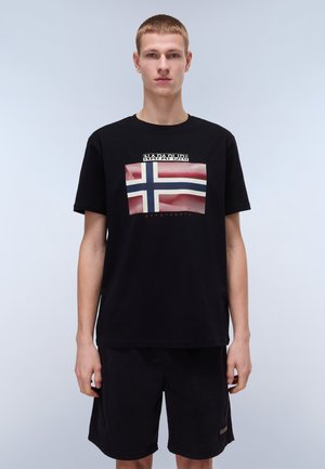 Camiseta de algodón negra con un gráfico de la bandera noruega sobre un fondo con puntos y texto arriba. Combinada con pantalones cortos negros.