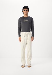 Grå langærmet skjorte med hvidt logo, kombineret med cremefarvede ribbede bukser og lyse sneakers med en brun sål. Solbriller inkluderet.