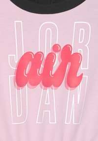 Fioletowa tkanina z czarnym dekoltem posiada wyrazisty, puszysty czerwony tekst "air" nałożony na białe kontury, które tworzą napis "JORDAN."