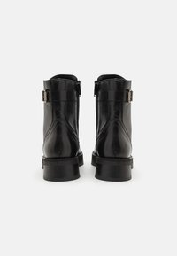 Botas de tobillo de cuero negro con un acabado suave, cremalleras traseras y un detalle de hebilla. Tacones bajos y gruesos con costuras reforzadas en las uniones.